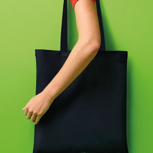 Pu&ograve; includere: Una borsa tote nera con manici lunghi &egrave; mostrata su uno sfondo verde brillante. La borsa &egrave; rettangolare e sembra essere fatta di un tessuto robusto. I manici sono dello stesso colore della borsa. Si vede il braccio e la mano di una persona che tiene la borsa.