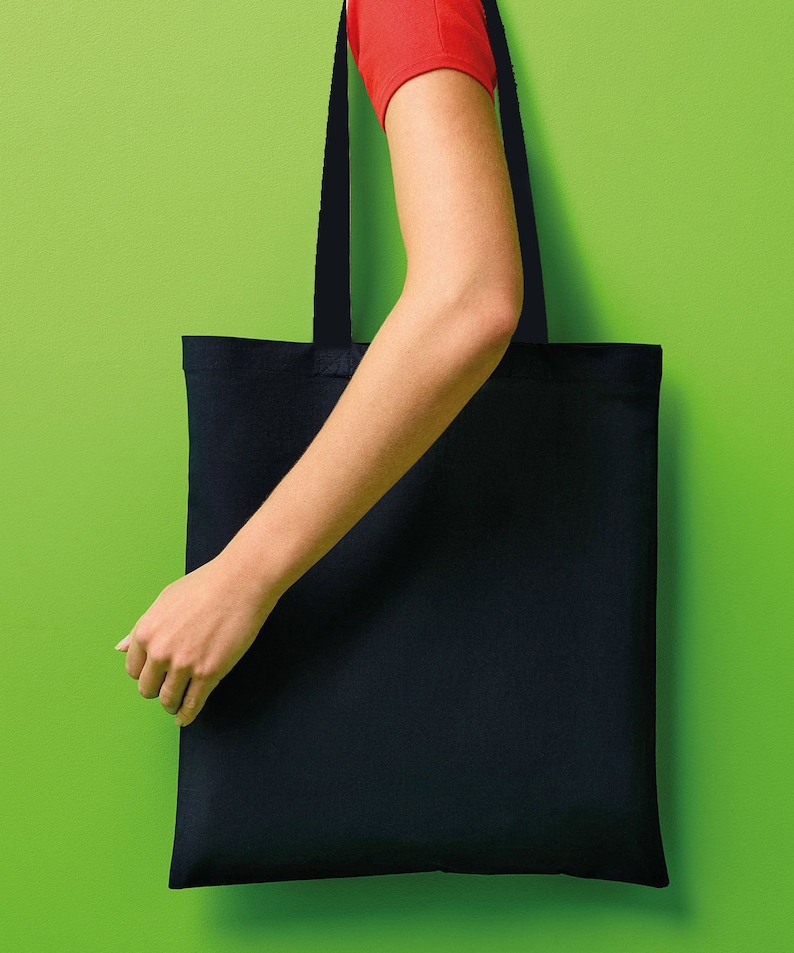 Pu&ograve; includere: Una borsa tote nera con manici lunghi &egrave; mostrata su uno sfondo verde brillante. La borsa &egrave; rettangolare e sembra essere fatta di un tessuto robusto. I manici sono dello stesso colore della borsa. Si vede il braccio e la mano di una persona che tiene la borsa.