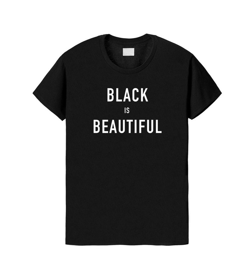 Puede incluir: Una camiseta negra de manga corta con el texto blanco "BLACK IS BEAUTIFUL" impreso en una fuente sans-serif en negrita en el centro del pecho. La prenda tiene un cuello redondo cl&aacute;sico y un corte est&aacute;ndar sobre un fondo liso.