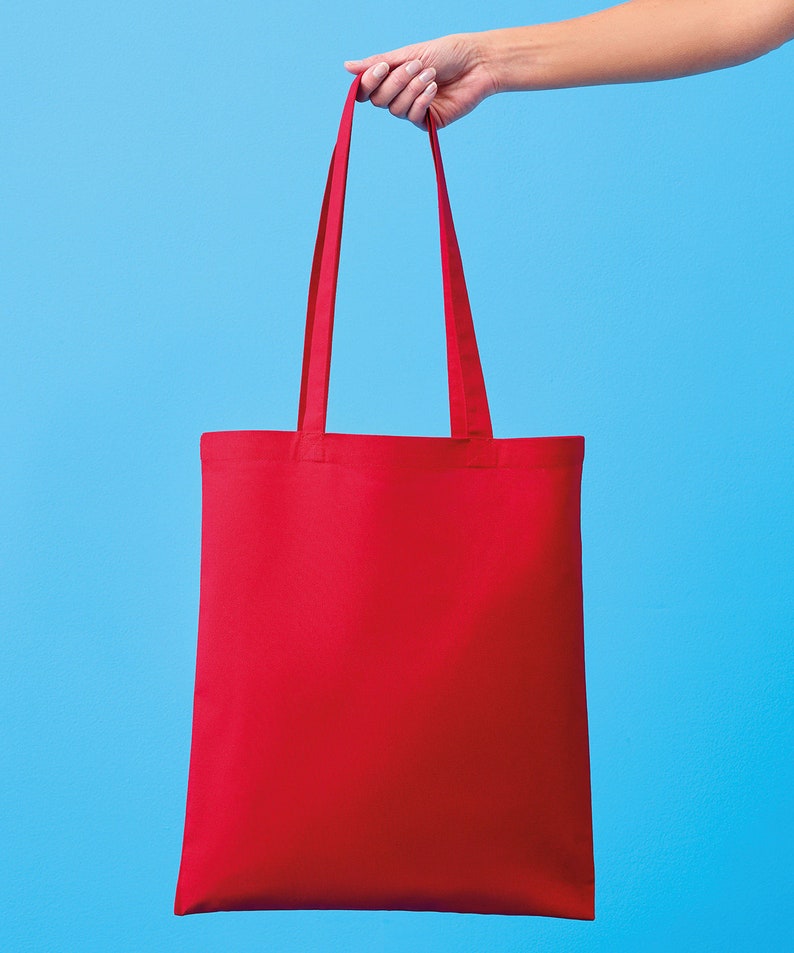 Pu&ograve; includere: Una borsa tote rossa tinta unita con lunghe cinghie &egrave; tenuta su uno sfondo azzurro. La borsa &egrave; rettangolare e sembra essere fatta di un tessuto robusto. Le cinghie sono dello stesso colore rosso della borsa.