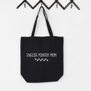 Puede incluir: Bolsa de tela negra con texto blanco que dice "English Pointer Mom" y una fila de huellas de patas.