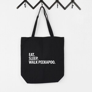 Può includere: Borsa tote in tela nera con testo bianco che dice "Eat. Sleep. Walk Peekaboo."