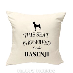 May include: A white throw pillow with black text that reads "This seat is reserved for the Basenji" and a black silhouette of a Basenji dog.