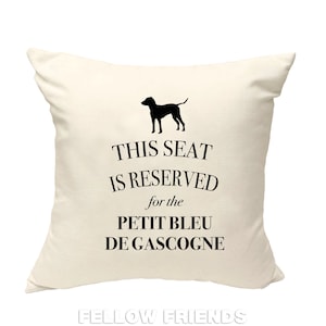 May include: A white throw pillow with black text that reads "This seat is reserved for the Petit Bleu de Gascogne". A black silhouette of a dog is above the text.