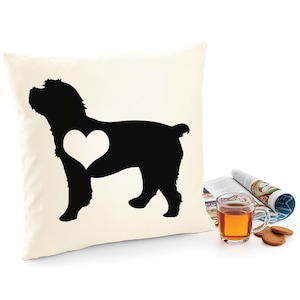 May include: A white pillow with a black silhouette of a dog with a heart in its chest. The dog is standing on all four legs and is facing to the right. The pillow is on a white surface.