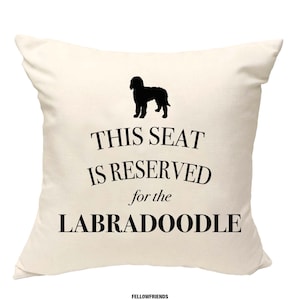 May include: A white throw pillow with black text that reads "This seat is reserved for the Labradoodle". A black silhouette of a Labradoodle is above the text.