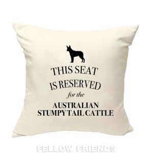 May include: A white throw pillow with black text that reads "This seat is reserved for the Australian Stumpy Tail Cattle". A black silhouette of an Australian Stumpy Tail Cattle dog is above the text.