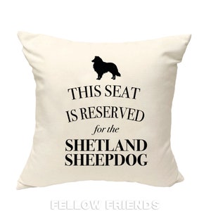 Könnte beinhalten: Ein weißes Kissen mit schwarzem Text, der "Dieser Platz ist für den Shetland Sheepdog reserviert" lautet. Oberhalb des Textes befindet sich eine schwarze Silhouette eines Shetland Sheepdogs.