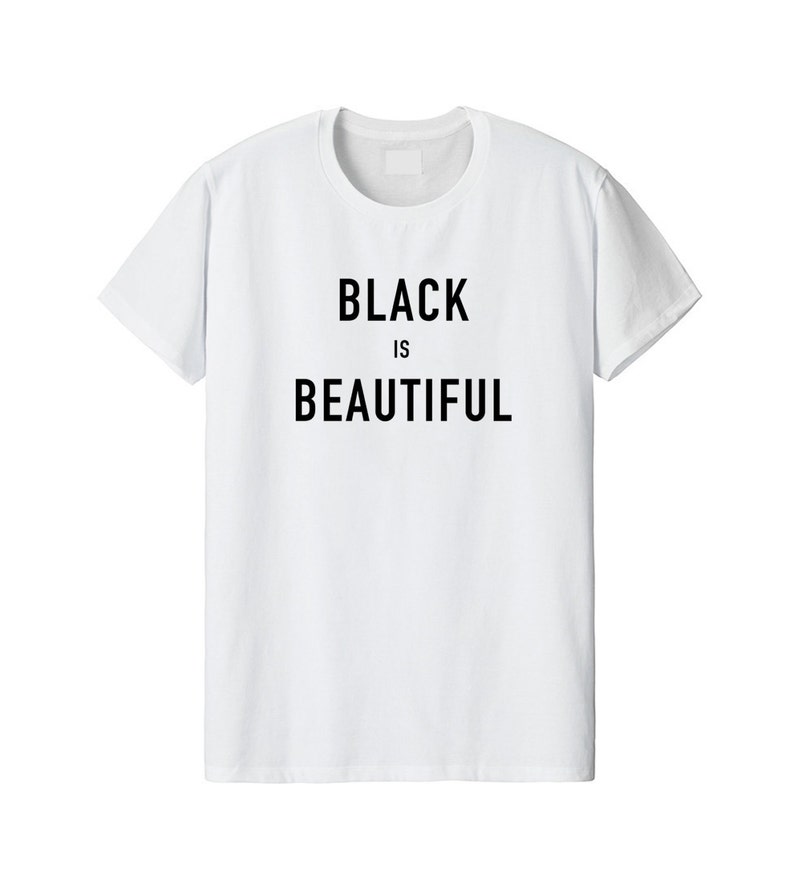 Puede incluir: Una camiseta blanca de manga corta con el texto BLACK IS BEAUTIFUL impreso en letras may&uacute;sculas negras y negritas en el centro del pecho. La prenda tiene un cuello redondo cl&aacute;sico y un dobladillo recto para un aspecto limpio.