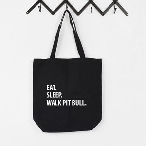 May include: Black canvas tote bag with white text that reads "Eat. Sleep. Walk Pit Bull."