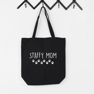 May include: Black canvas tote bag with white text that reads "Staffy Mom" and a row of white paw prints.