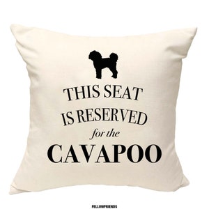 Op de afbeelding: Wit kussen met zwarte tekst die "Deze stoel is gereserveerd voor de Cavapoo" luidt en een zwart silhouet van een Cavapoo-hond.