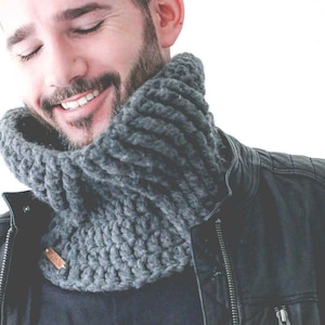 May include: A man wearing a gray knitted neck warmer and a black leather jacket. The neck warmer is thick and has a chunky knit texture.