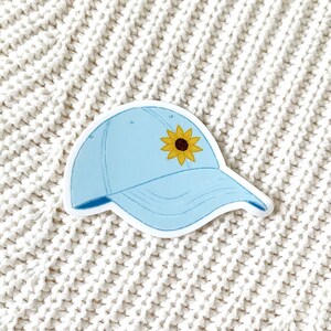 May include: A light blue baseball cap with a yellow sunflower on the front.