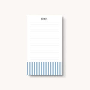 Könnte beinhalten: Rechteckiger Notizblock mit liniertem weißem Papier. Der untere Teil des Notizblocks weist ein blau-weißes Streifenmuster auf. Das Wort "notes" ist in kleiner, dunkler Schrift oben auf dem Notizblock aufgedruckt.