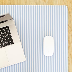 May include: A white laptop and mouse rest on a blue and white striped desk mat. The mat is rectangular and has vertical stripes. The laptop is open, displaying the keyboard. The mouse is oval-shaped.