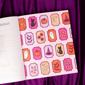 May include: Open book with a pink page featuring Halloween-themed illustrations. The illustrations include a black cat, pumpkins, ghosts, bats, and witch hats. The illustrations are in orange, pink, and purple.
