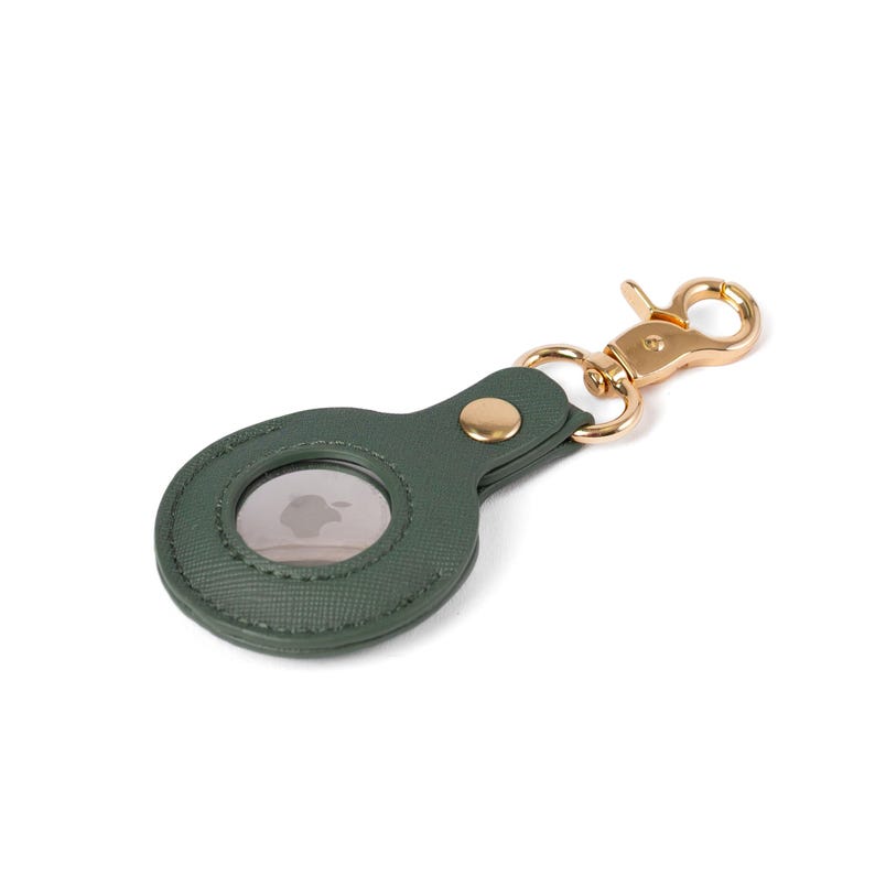 May include: A dark green textured faux leather protective case for an Apple AirTag, featuring a circular cutout to display the device, a gold-toned metal snap button closure, and a matching gold-toned lobster claw clasp for attachment.