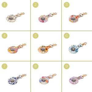 May include: Nine floral-patterned keychains with gold-colored hardware. Each keychain has a circular design with a different floral pattern in various colors, including white, pink, orange, blue, and purple. The keychains are arranged in a grid.
