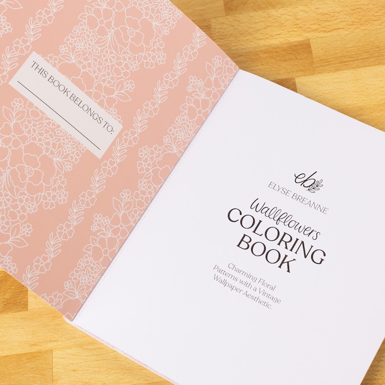 May include: Open coloring book with a peach cover featuring white floral patterns and the text "THIS BOOK BELONGS TO:". The right page displays "Wallflowers COLORING BOOK" by Elyse Breanne, with "Charming Floral Patterns with a Vintage Wallpaper Aesthetic."