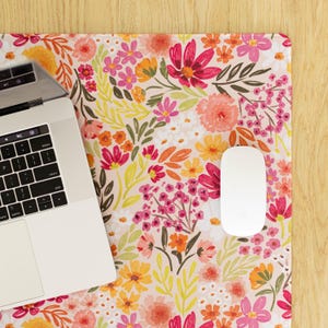 May include: A floral mousepad with a vibrant pattern of pink, orange, and yellow flowers on a light pink background. A white computer mouse and a laptop are on the mousepad. The laptop keyboard is visible.