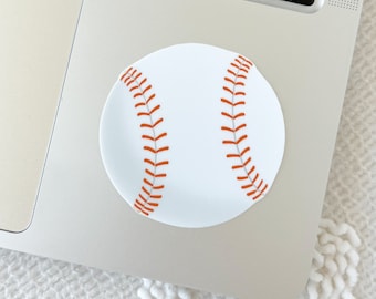 May include: A white baseball with orange stitching. The baseball is on a silver laptop.