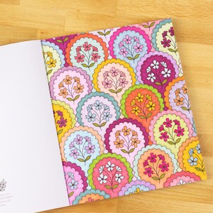 May include: Open coloring book with a colorful floral pattern. The design features scalloped circles in various colors like pink, orange, yellow, and blue, each containing a cluster of flowers. The open page reveals a blank white page.