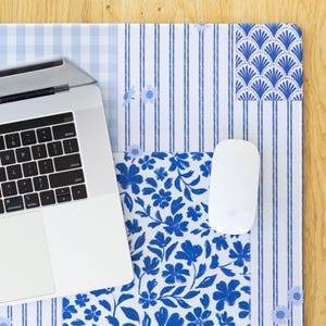 Puede incluir: Alfombrilla de escritorio con estampado azul y blanco con un portátil y un ratón. La alfombrilla presenta un diseño de patchwork con estampados florales, de rayas y de cuadros. El portátil es plateado y el ratón es blanco. La alfombrilla está sobre una superficie de madera.