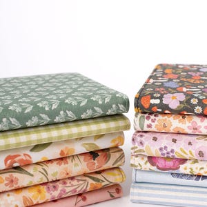 以下が含まれることがあります： 花柄と模様のデザインが施された布製の本の2つのスタック。左側のスタックは、緑、白、桃色の花柄を特徴とし、右側のスタックは、黒の花柄のデザインと、ピンクと青のストライプ柄を特徴としています。