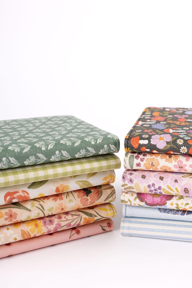 May include: Two stacks of fabric with floral and patterned designs. One stack features a green floral pattern, a green and white gingham, and floral prints in peach and pink. The other stack has a black floral, pink floral, and blue striped fabric.