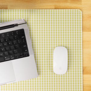 May include: A laptop, a white wireless mouse, and a yellow and white checkered mousepad are on a wooden surface. The laptop is silver with a black keyboard. The mouse is oval-shaped with a smooth surface. The mousepad has a gingham pattern.