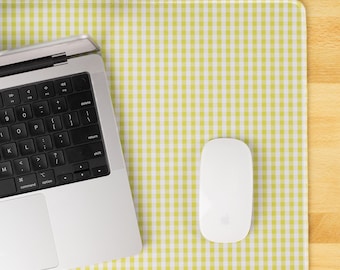Pode incluir: Um laptop prateado, um rato sem fios branco e um tapete de rato xadrez amarelo e branco estão numa superfície de madeira. O laptop tem um teclado preto. O rato é oval e tem uma superfície lisa. O tapete tem um padrão xadrez.