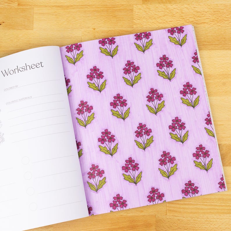 May include: Open workbook with the word "Worksheet" visible. The right page features a repeating pattern of pink flowers with green leaves on a light purple background. The left page has lines for coloring information.