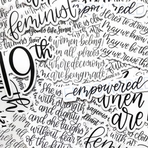 May include: A collection of black and white stickers with feminist and empowering messages. The stickers feature phrases like "feminist", "she is empowered", "women belong in all places where decisions are being made", and "may we know our future".