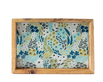 May include: Rectangular wooden tray with a floral pattern. The tray has a light brown wooden frame and a patterned interior with blue, yellow, and green flowers and leaves on a white background. The tray is rectangular.