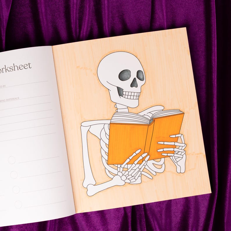 May include: Open notebook with a skeleton illustration reading an orange book. The skeleton is white with black eye sockets and a detailed rib cage. The notebook is open to a worksheet page.