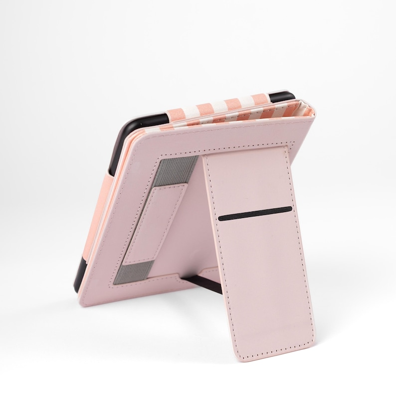 May include: A pink tablet case with a stand. The case is open, revealing a black tablet. The interior lining features a white and pink striped pattern. The stand is also pink and has a black horizontal accent.
