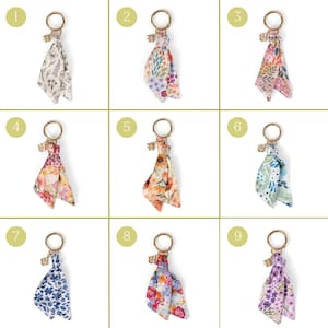 May include: Nine keychains with floral patterned fabric tassels. Each keychain has a gold-colored ring and a small charm. The fabric patterns include various colors like white, blue, pink, orange, and purple, with different floral designs.