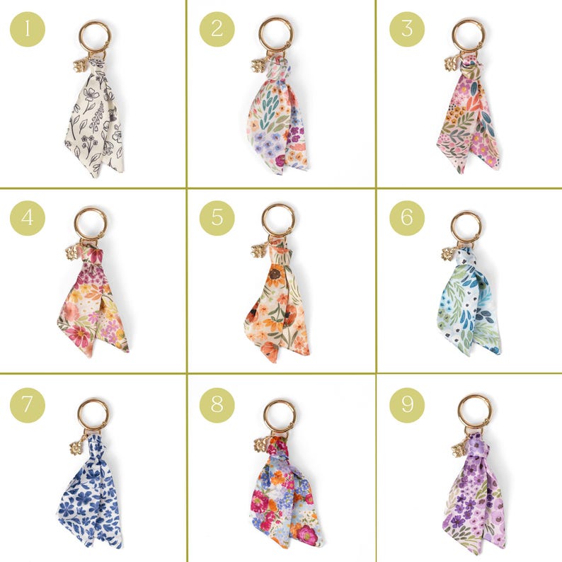 May include: Nine keychains with floral patterned fabric tassels. Each keychain has a gold-colored ring and a small charm. The fabric patterns include various colors like white, blue, pink, orange, and purple, with different floral designs.