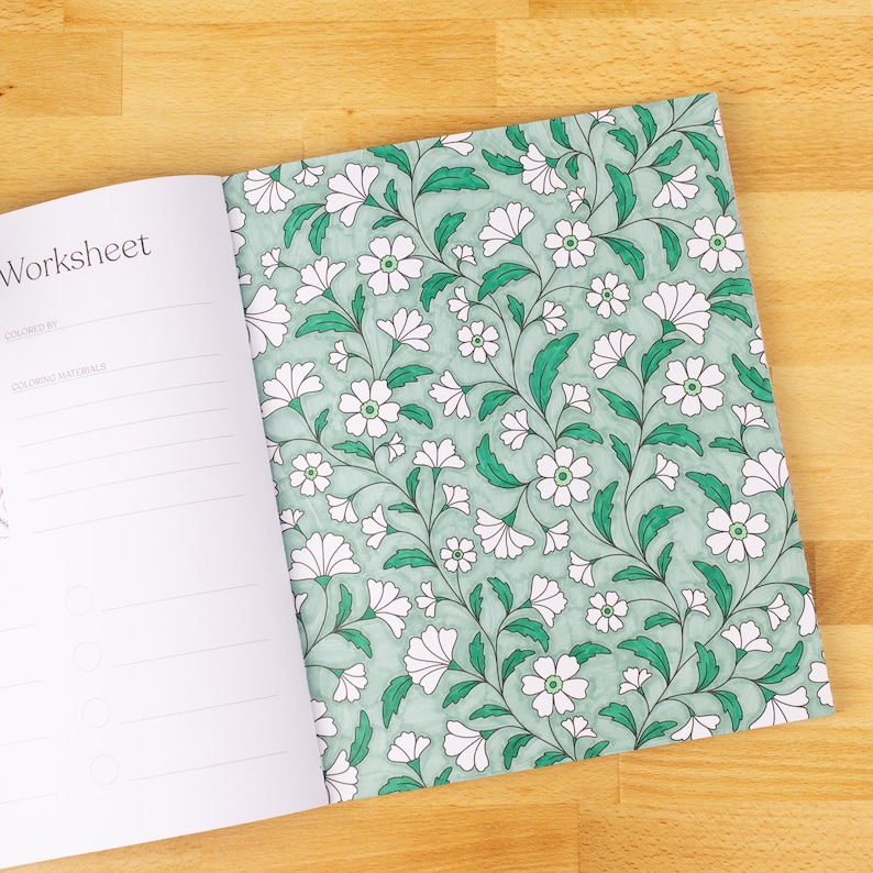 May include: Open coloring book with a floral pattern on the right page and the word "Worksheet" on the left page. The floral design features white flowers with green centers and green leaves on a light teal background.