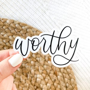 May include: White sticker with the word "worthy" written in black cursive script.