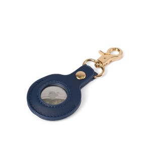 May include: A navy blue circular protective case for a tracking device, featuring a textured surface, a gold-toned metal snap button, and a matching gold-toned lobster claw clasp attached to a small metal ring for secure fastening to items.