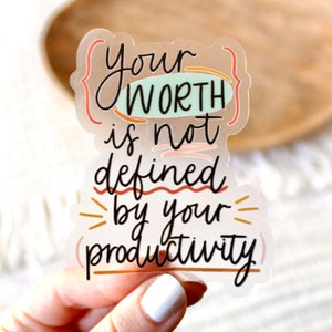 May include: A clear sticker with the text "Your worth is not defined by your productivity" in black script. The text is surrounded by colorful abstract shapes.