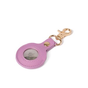 May include: A lavender-colored circular protective case for a tracking device, featuring a textured surface and a gold-toned metal lobster clasp attached by a matching lavender strap with a single gold-toned rivet securing the loop.