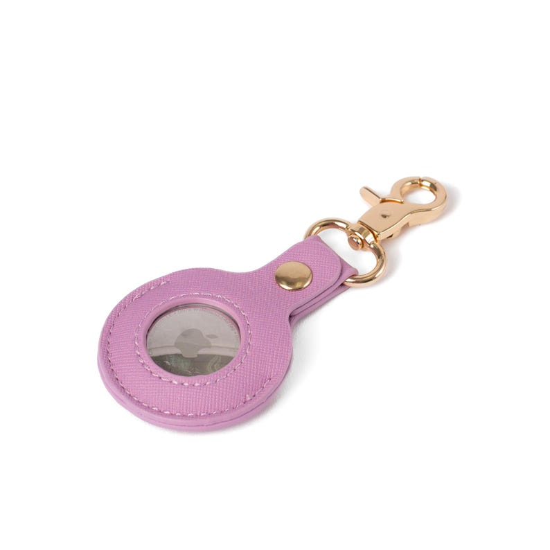 May include: A lavender-colored circular protective case for a tracking device, featuring a textured surface and a gold-toned metal lobster clasp attached by a matching lavender strap with a single gold-toned rivet securing the loop.