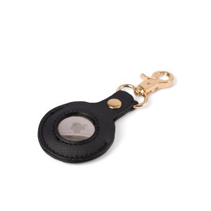 May include: A black textured protective case for a circular tracking device, featuring a gold-toned metal snap button closure and a matching gold-toned lobster claw clasp attached to a small metal ring for secure fastening to keys or bags.