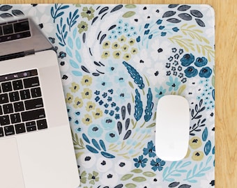 May include: A floral patterned mousepad with a laptop and a white mouse. The mousepad features a light blue background with a repeating pattern of blue, green, and white flowers and leaves. The laptop is silver and the mouse is white.