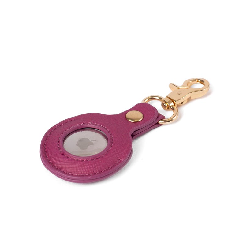 May include: A magenta faux leather protective case for an Apple AirTag featuring a textured surface, a gold-toned metal snap button closure, and a matching gold-toned lobster claw clasp attached to a circular metal ring for secure fastening.