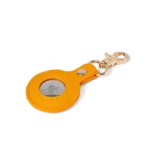 May include: A bright yellow circular protective case for a tracking device, featuring a textured finish, a central circular cutout, a gold-toned metal snap button, and a matching gold-toned lobster claw clasp attached by a metal ring.