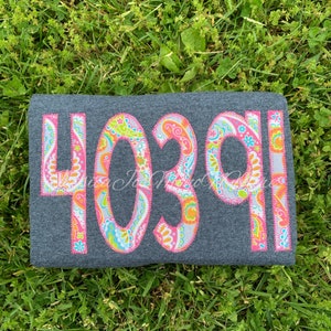 May include: A dark gray t-shirt with the number 4039 sewn on in pink, white, and green paisley fabric.
